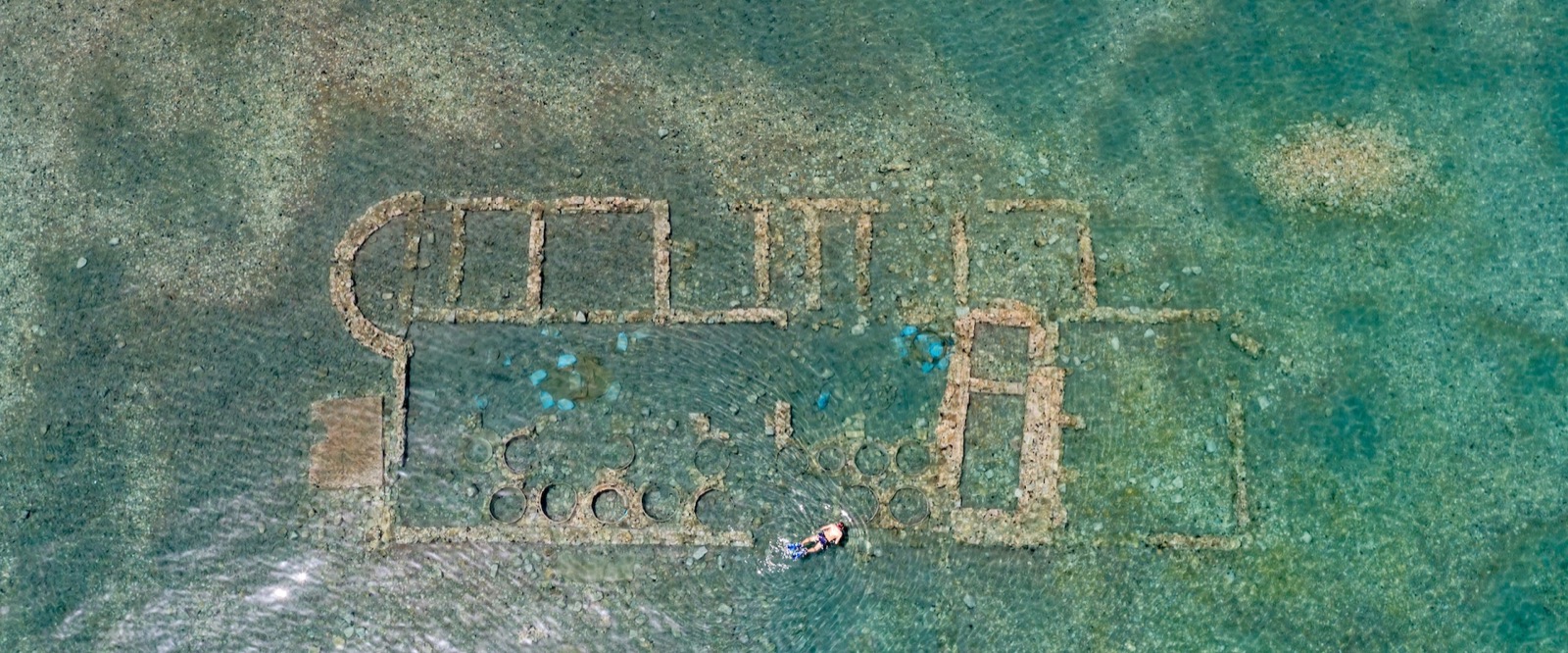 A snorkeller above submerged stone walls and storage jars near Epidaurus